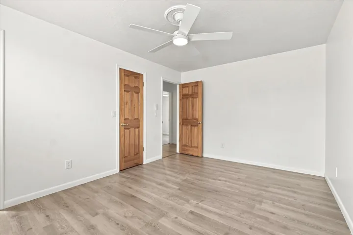 Wood-finish flooring, white walls, and a ceiling fan with integrated lighting