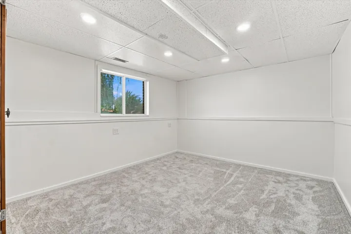 Recessed lighting, drop ceiling, wall paneling, window, and grey patterned carpeting