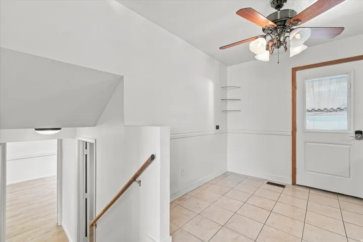 Tiled flooring, wood-finish ceiling fan with integrated lighting, wood-finish railing, and white wall paneling