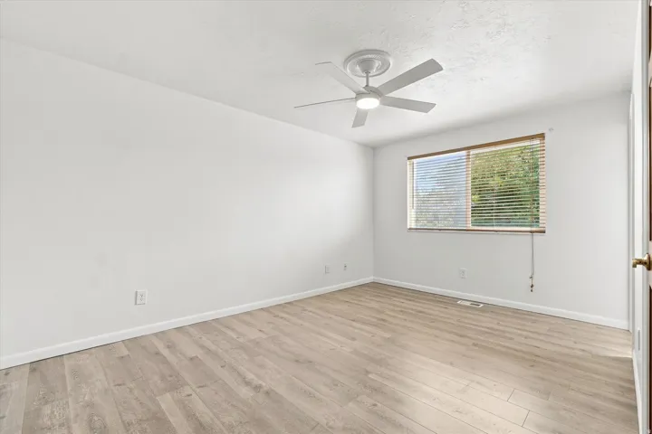 Wood-finish flooring, white walls, ceiling fan, and a window with blinds