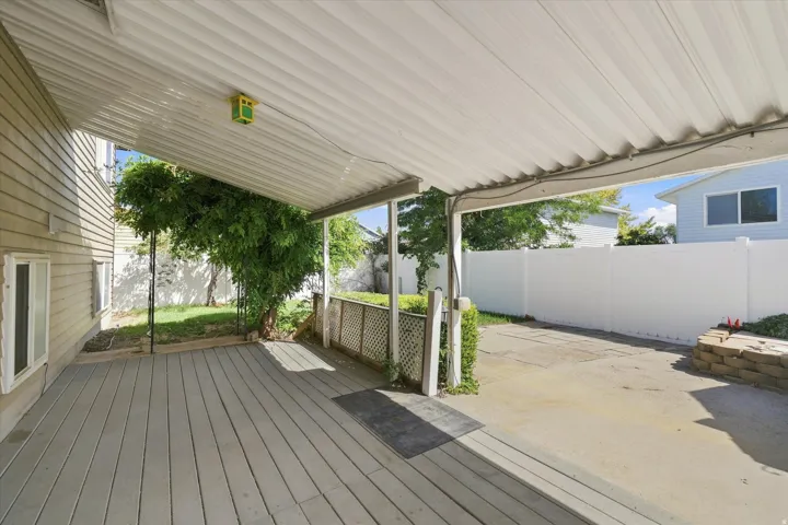 Covered patio with a composite deck, extending to a concrete pad, bordered by a white privacy fence