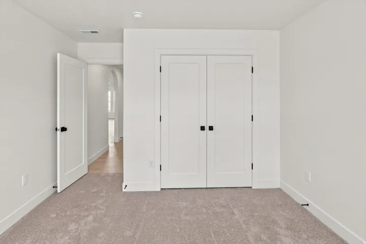 Plush carpet flooring, white walls, double closet doors with black hardware, and an open doorway leading to an arched hallway