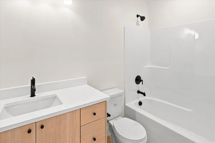 Bathroom featuring a light wood-finish vanity with a white countertop, an undermount sink, and matte black fixtures
