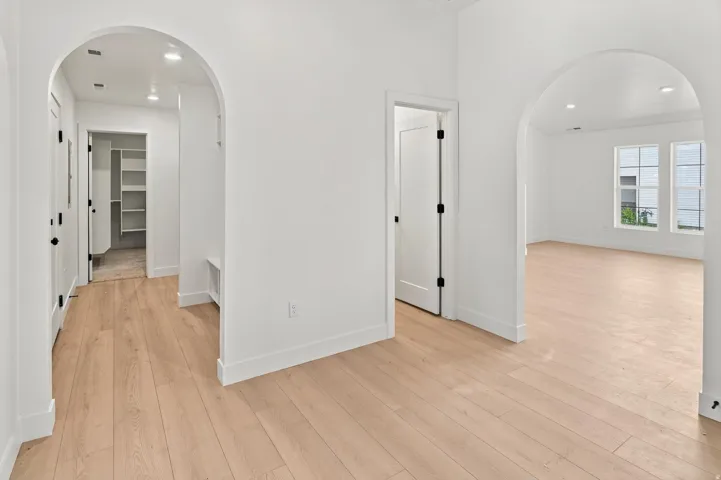 Light wood-finish flooring throughout, multiple arched doorways, white walls, recessed lighting, and a built-in shelving unit