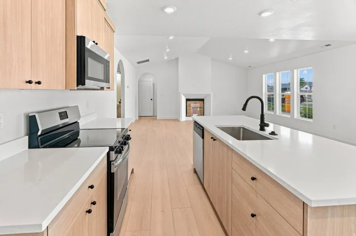 Kitchen with light wood-finish cabinetry, stainless steel appliances, solid surface countertops, and an undermount sink with a matte black faucet