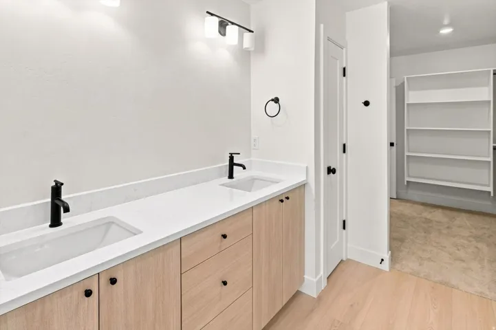 Double vanity with integrated sinks, light wood-finish cabinetry, quartz countertops, and matte black hardware