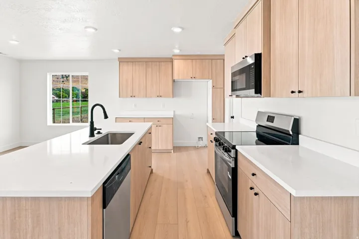 Kitchen featuring light wood-finish cabinetry, white countertops, stainless steel appliances, and a central island with an integrated sink
