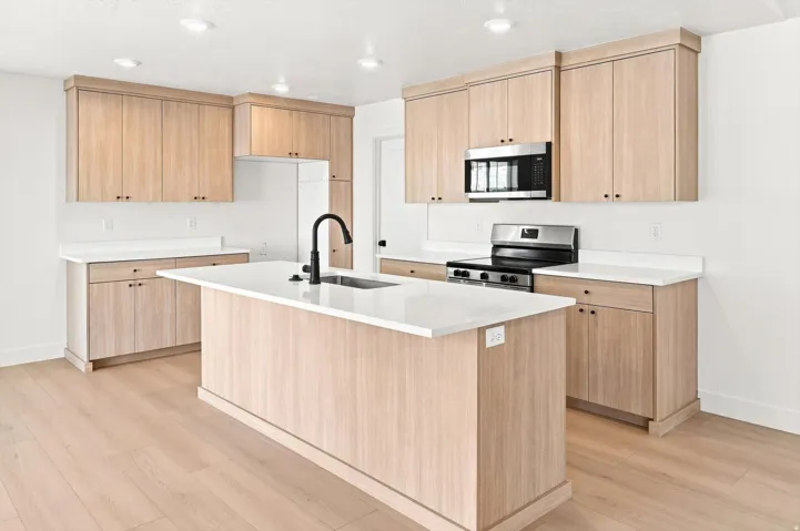Kitchen featuring light wood-finish cabinetry, white countertops, stainless steel appliances, a center island with sink, and wood-finish flooring