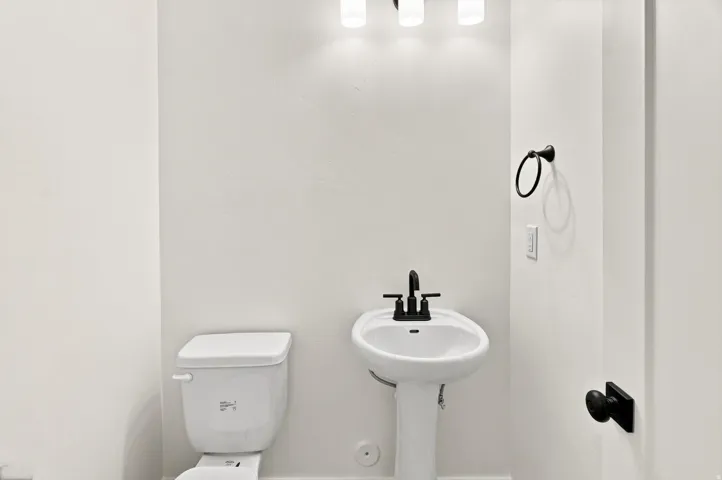 Pedestal sink with matte black faucet, wall-mounted light fixture, and matte black door hardware