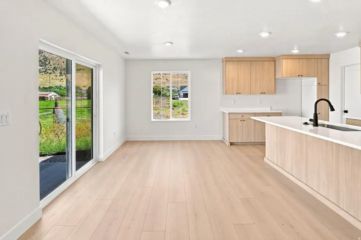 Light wood-finish flooring throughout, modern kitchen with light wood cabinetry, white countertops, and a kitchen island with an integrated sink