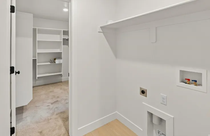 Laundry area with a built-in shelf, appliance hookups, and wood-finish flooring