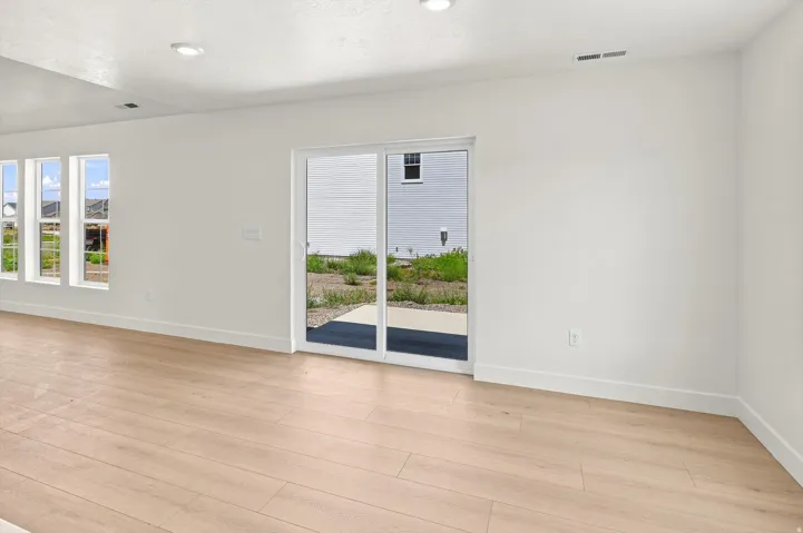 Light wood-finish flooring, white walls, multiple windows, recessed lighting, and a glass sliding door