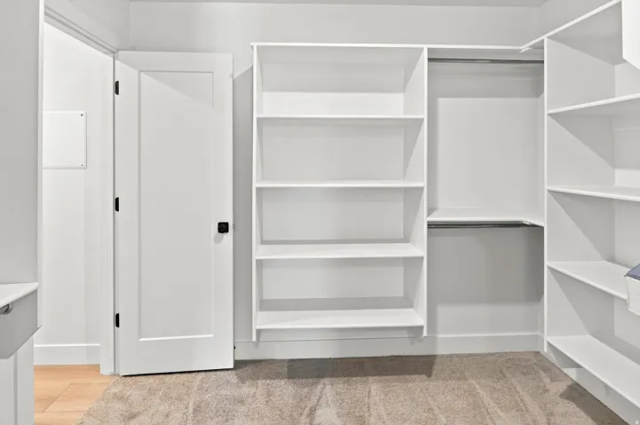 White built-in shelving, integrated hanging rods, and light-colored carpeting