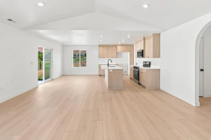 Vaulted ceiling, recessed lighting, wood-finish flooring, sliding glass door, and a kitchen island with sink
