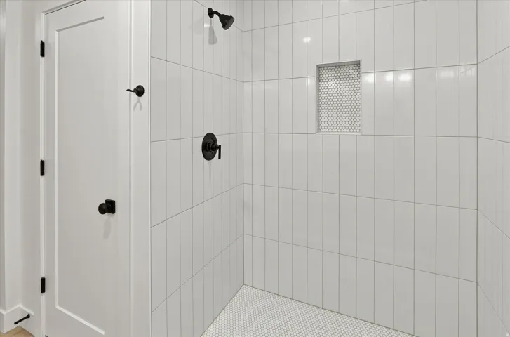 Walk-in shower featuring vertical subway tile, a recessed niche with mosaic tile, a matte black shower head, and a matching matte black shower control