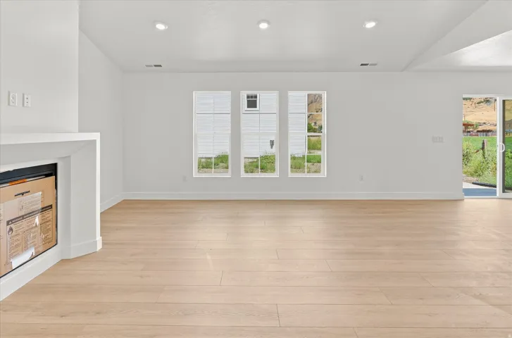 Recessed lighting, wood-finish flooring, three transom windows, white fireplace mantel, and sliding glass door