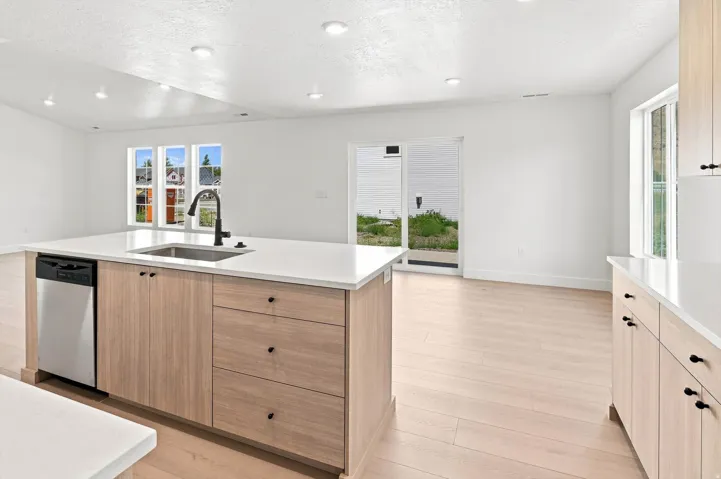 Kitchen island with light wood-finish cabinetry, integrated stainless steel dishwasher, and a black gooseneck faucet