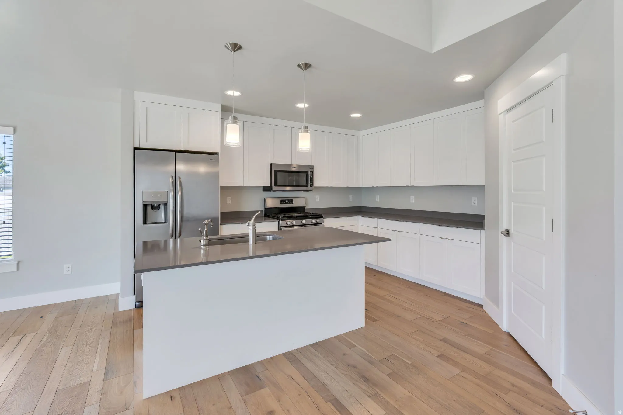 White cabinetry with dark countertops, stainless steel appliances, and wood-finish flooring