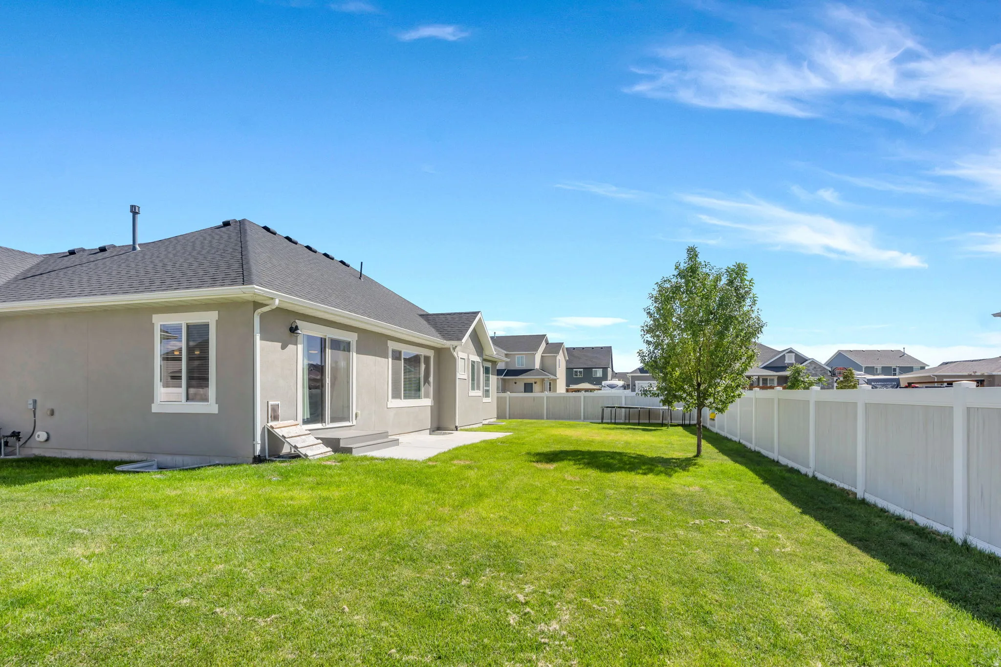Expansive backyard with a manicured lawn, established tree, and full privacy fencing