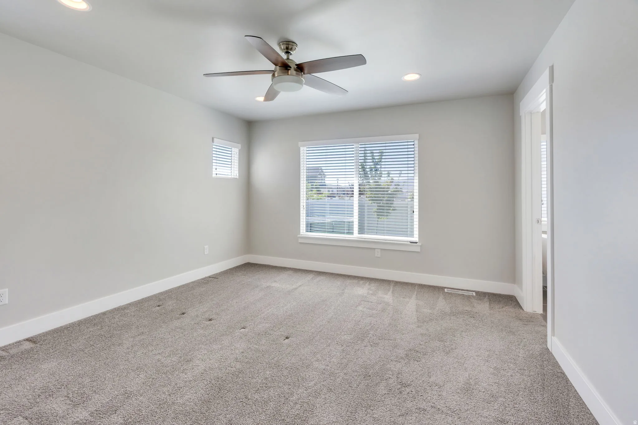 Spacious room featuring neutral carpeting, recessed lighting, a ceiling fan, and two windows with blinds