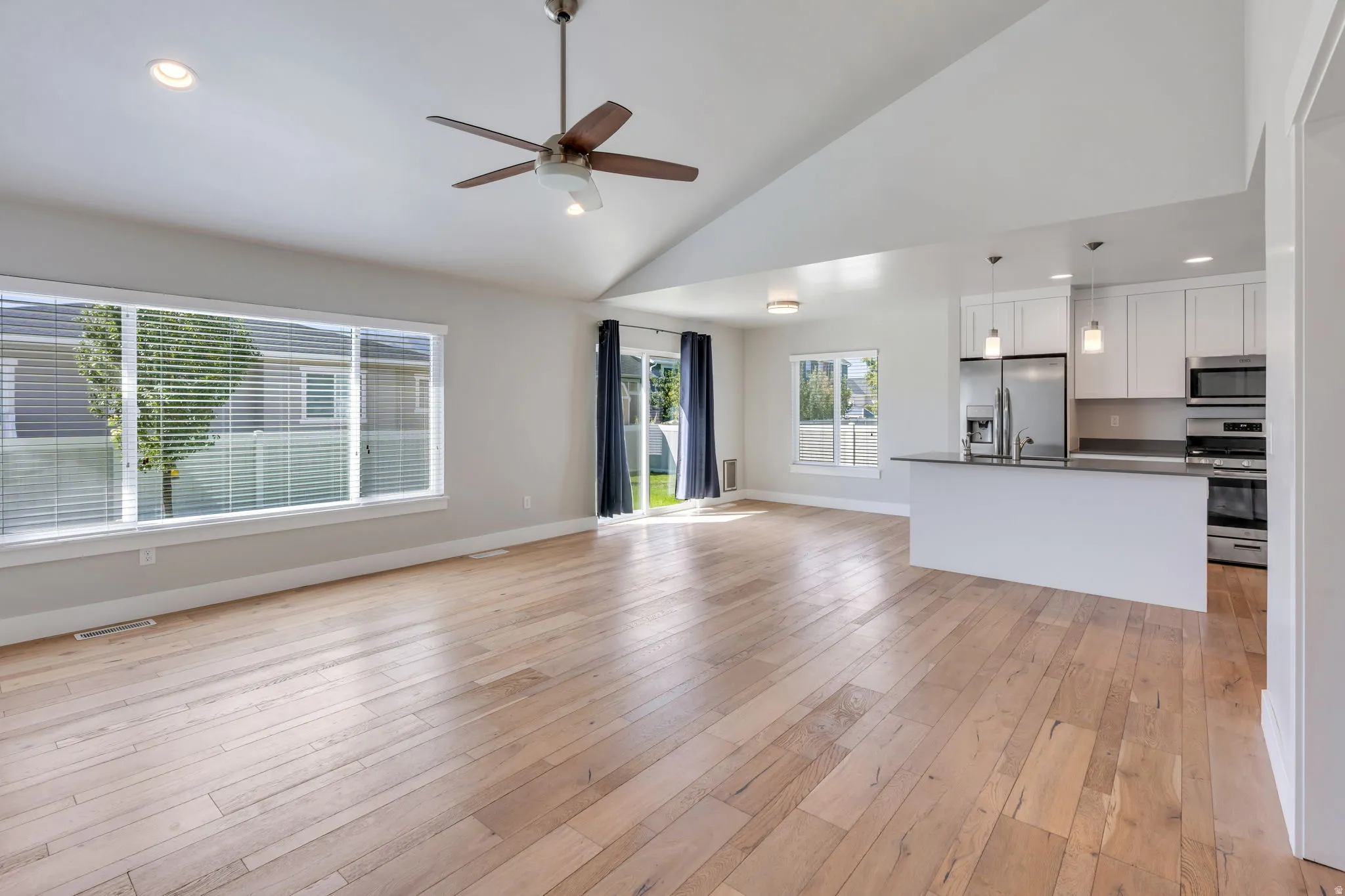 Vaulted ceiling with a ceiling fan, light wood-finish flooring, white cabinetry, stainless steel appliances, and a kitchen island with pendant lighting