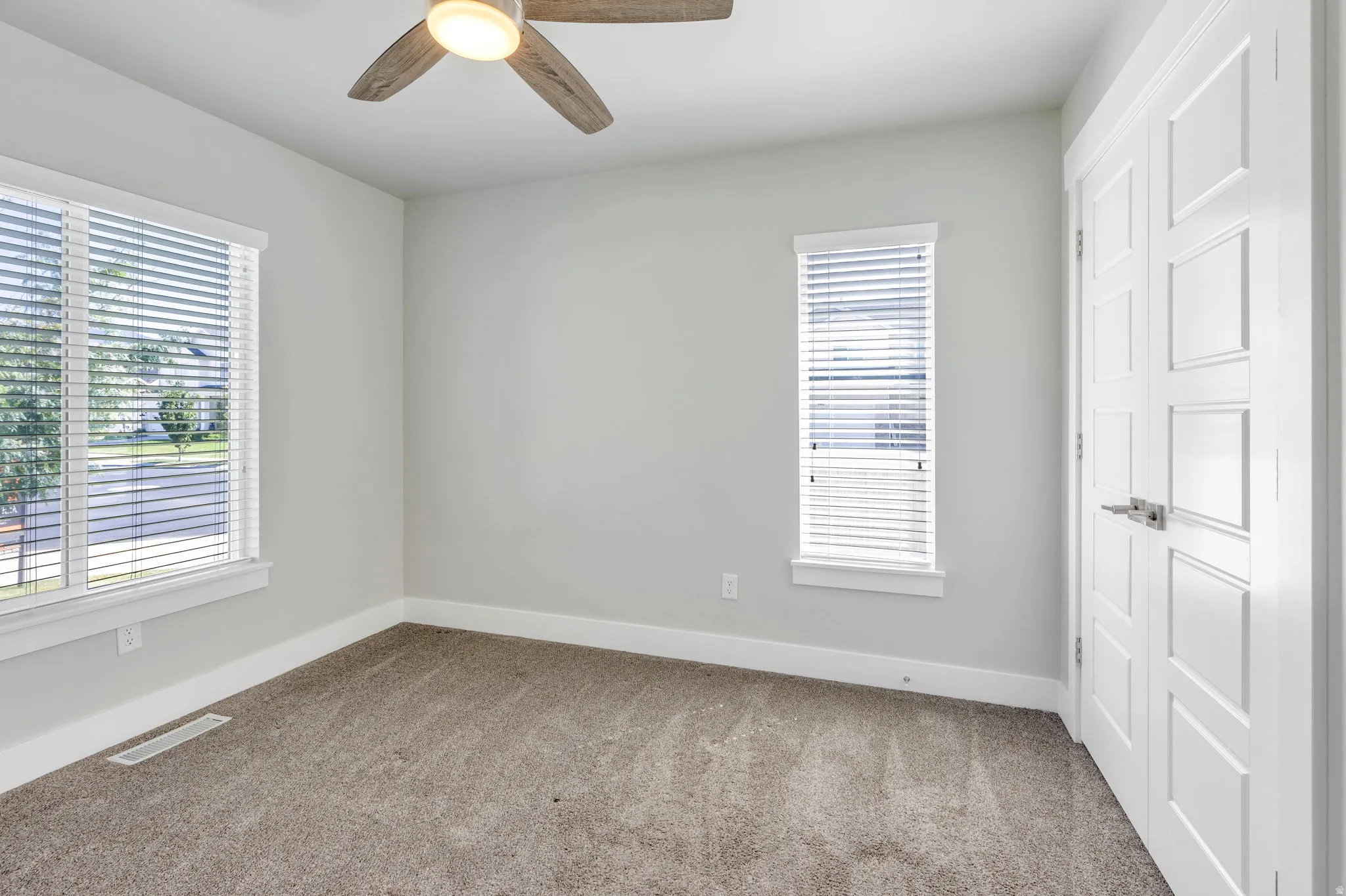 Plush carpeting, contemporary ceiling fan, two windows with blinds, and a white paneled door