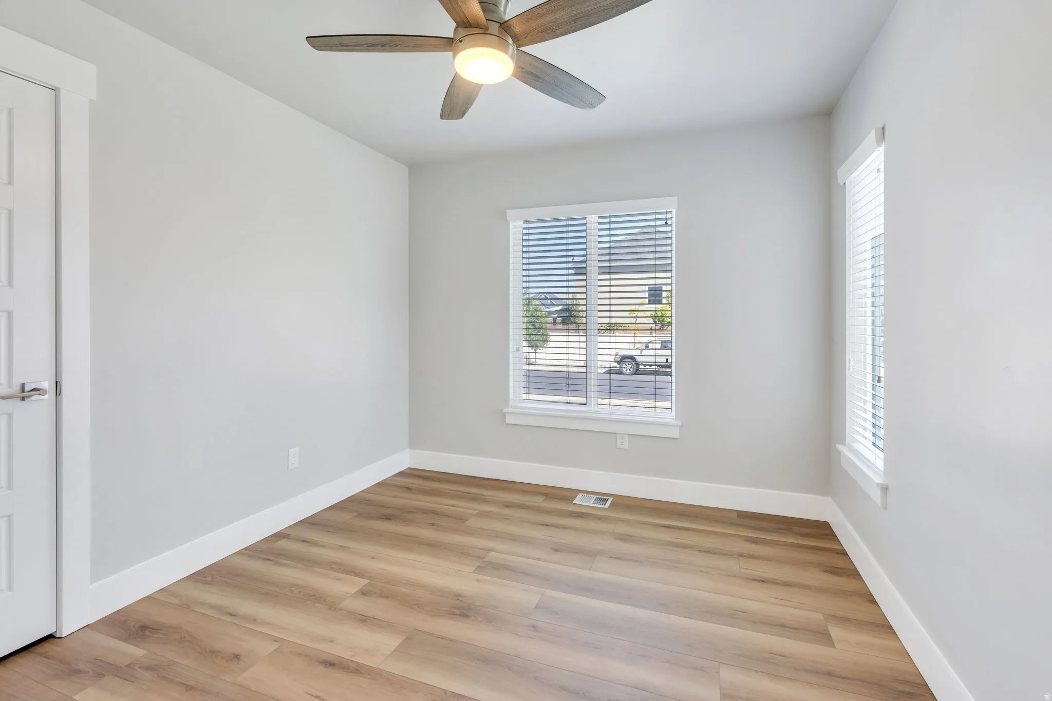 Wood-finish flooring, overhead lighting with a ceiling fan, and white window blinds