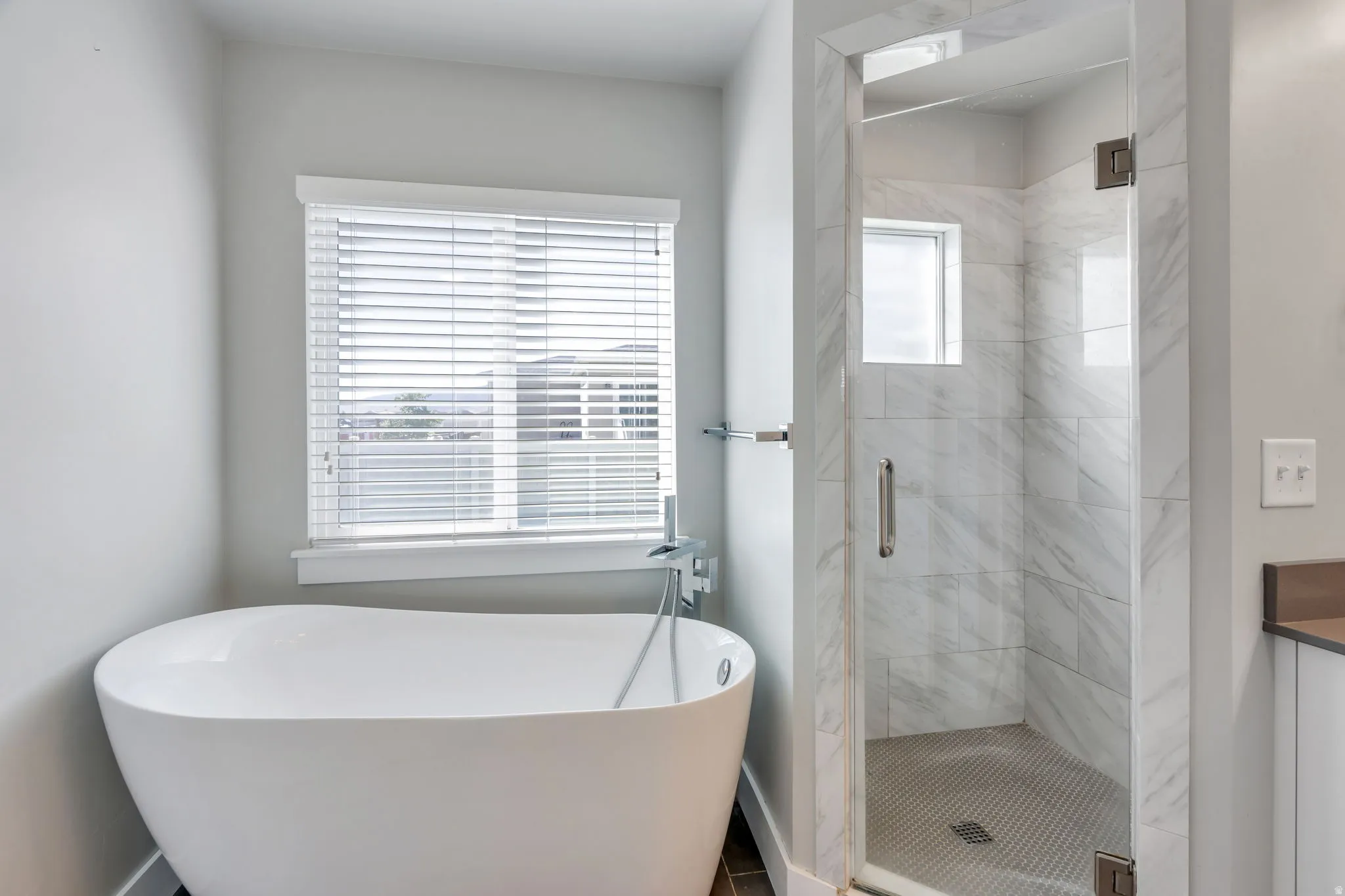 Freestanding soaking tub with a window, glass-enclosed shower with tiled walls, and a built-in shower niche