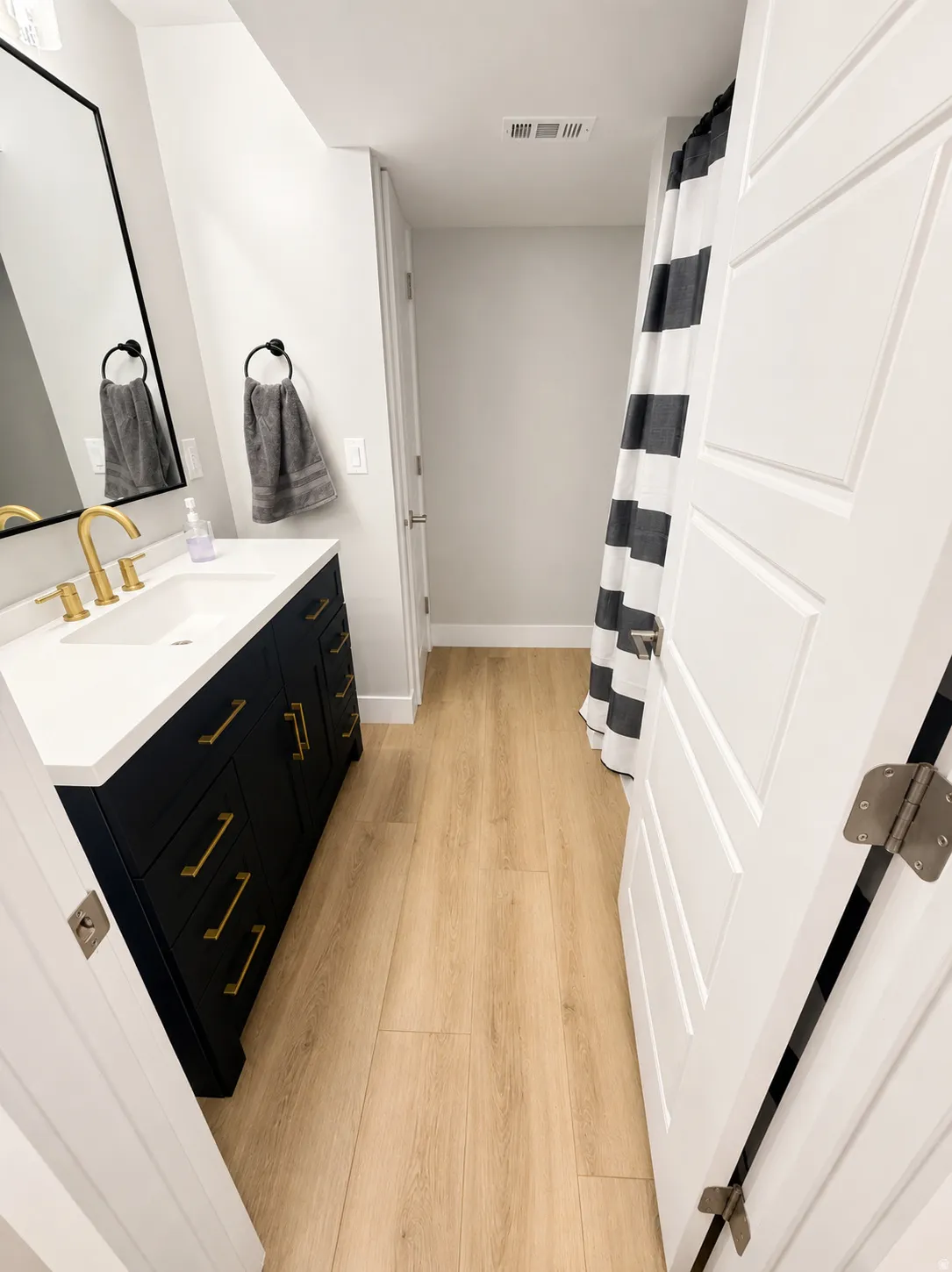 White quartz countertop with an undermount sink, a black vanity with gold-finish hardware, and wood-finish flooring