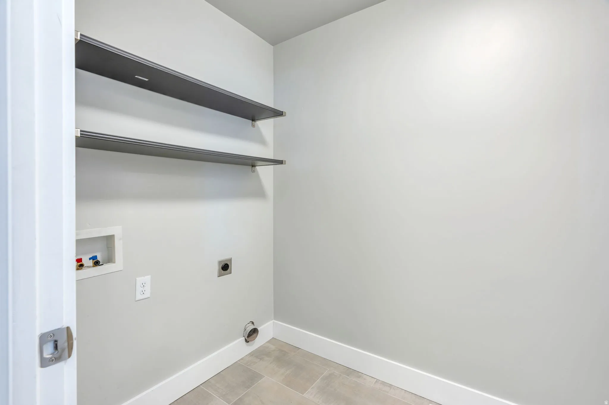 Laundry area featuring two wall-mounted shelves, a washer hookup, dryer vent, and tile flooring