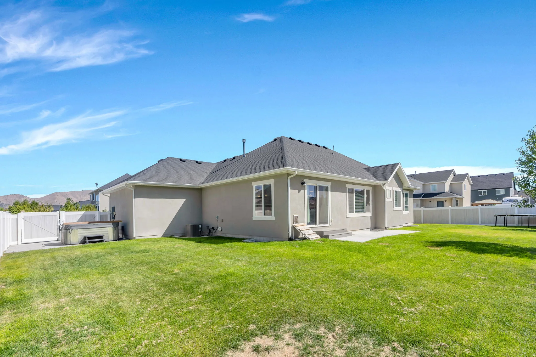 Expansive backyard with a manicured lawn, concrete patio, and white vinyl fencing