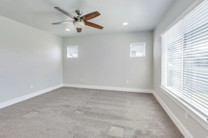 Recessed ceiling lighting, ceiling fan with wood-finish blades, multiple windows with blinds, and light gray wall paint