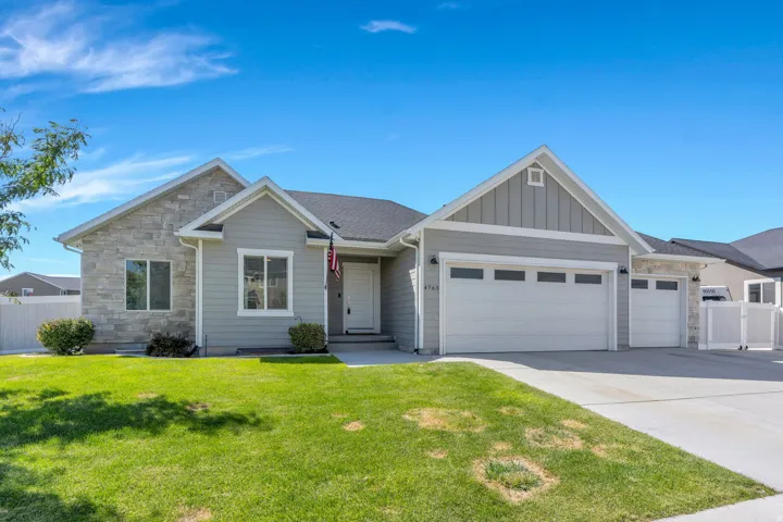 Siding exterior with stone accents, attached two-car garage, single-car garage, concrete driveway, and front lawn