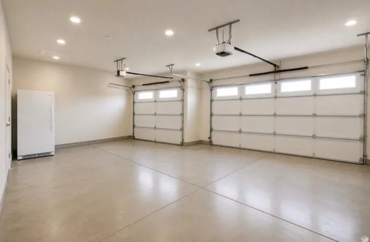 Two automatic garage doors with upper window panels, recessed ceiling lighting, and concrete flooring