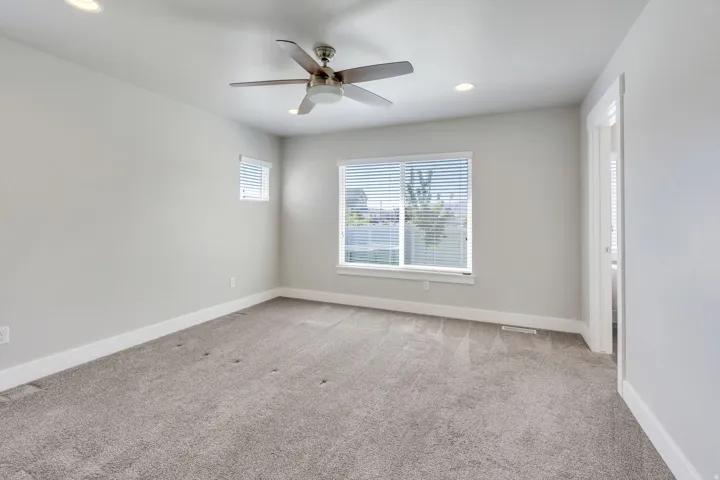 Spacious room featuring neutral carpeting, recessed lighting, a ceiling fan, and two windows with blinds