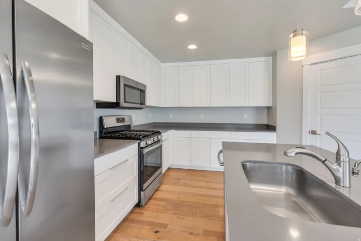 Stainless steel appliances, white cabinetry, undermount sink with brushed nickel faucet, light wood-finish flooring, and recessed lighting