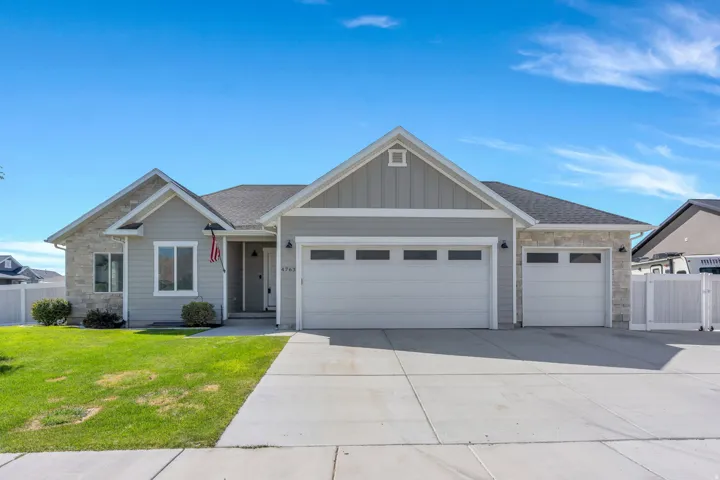 Exterior featuring light gray siding, stone accents, two-car garage, single-car garage, and a concrete driveway