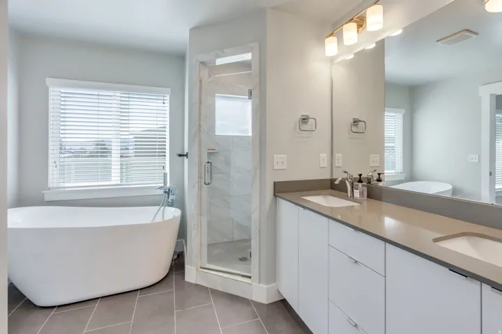 Freestanding soaking tub, walk-in shower with glass enclosure, dual vanity with undermount sinks, stone-finish countertops, and large mirror