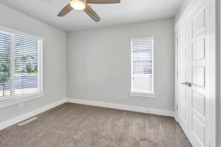 Plush carpeting, contemporary ceiling fan, two windows with blinds, and a white paneled door