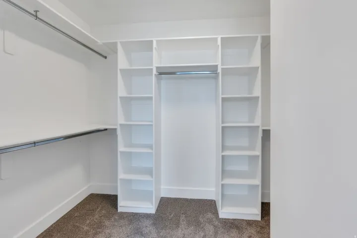 Built-in white shelving, integrated hanging rods, and carpeted flooring