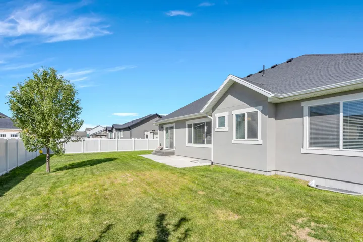 Expansive backyard featuring a manicured lawn, established tree, concrete patio, and a privacy fence