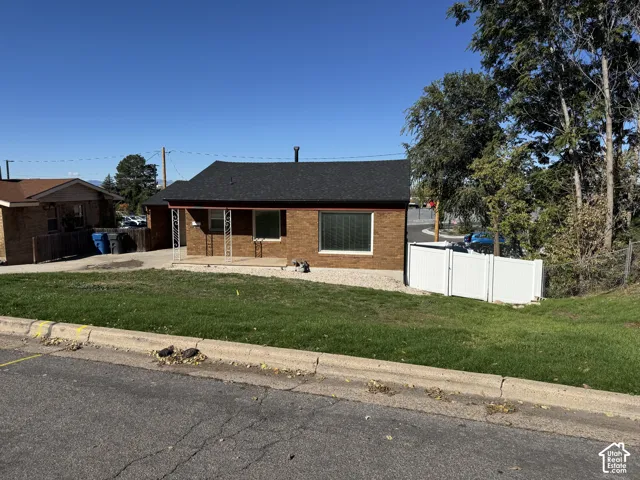 Single-story brick exterior featuring a dark asphalt shingle roof, covered front porch with decorative iron columns, and white vinyl privacy fencing