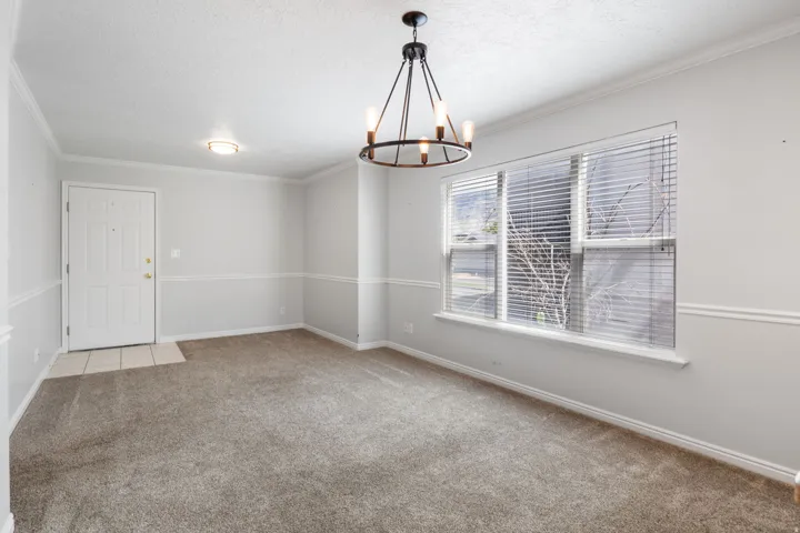 Spacious room featuring carpeting, a prominent window with blinds, and a stylish chandelier
