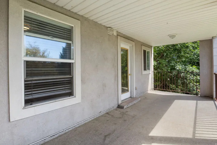 Covered concrete patio with a white ceiling, exterior wall sconce, and metal railing