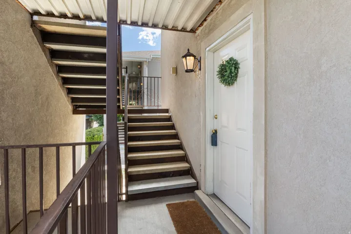 Exterior entry featuring a white paneled door, mounted outdoor light fixture, and textured stucco finish