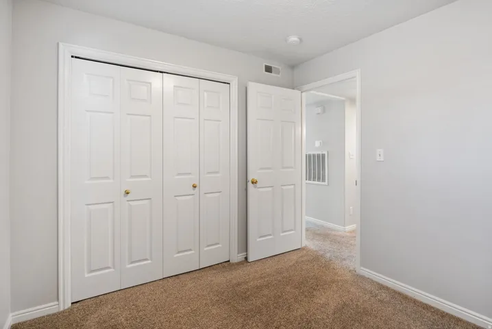 White bifold closet doors with brass hardware, light gray wall paint, and brown carpet flooring