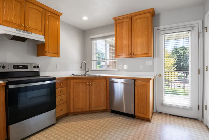 Kitchen featuring wood cabinetry, stainless steel appliances, a corner sink with a window, and a door with integrated blinds