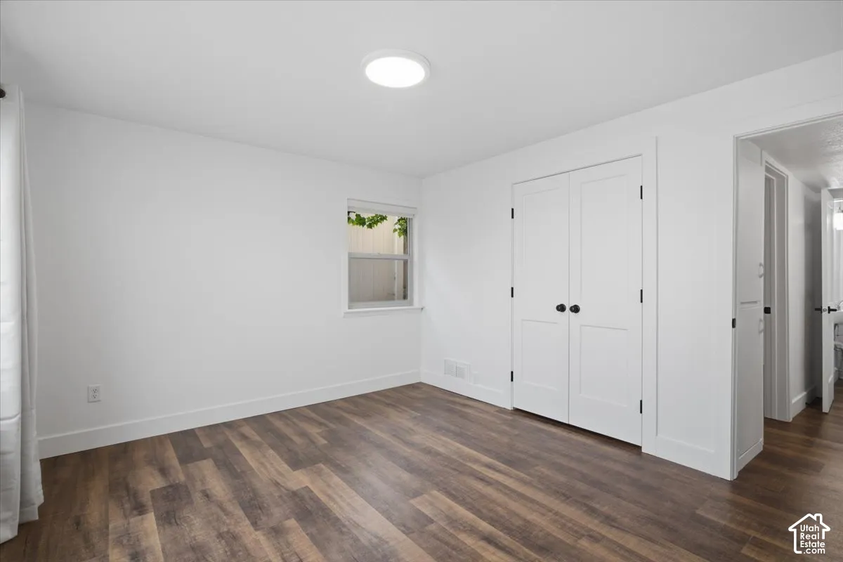 Wood-finish flooring with white baseboards, a window, and a built-in closet with panel doors