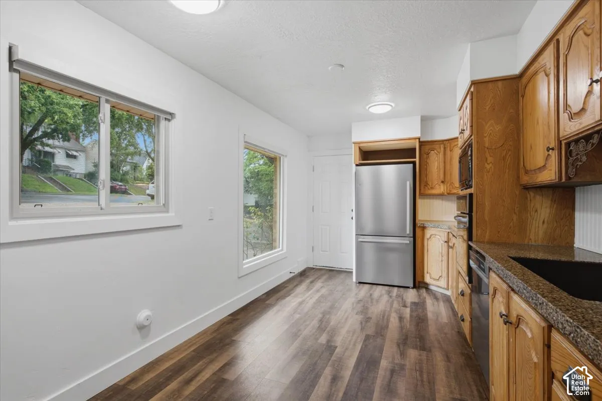 Kitchen space featuring wood-finish flooring, two large windows, wood cabinetry, granite-style countertops, and stainless steel appliances