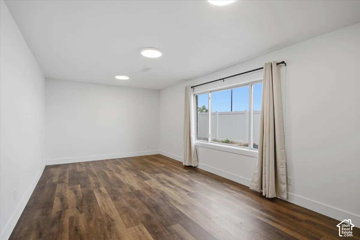 Recessed lighting, wood-finish flooring, white walls, and a large window with window treatments